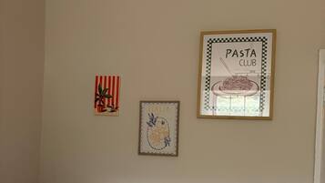 A room with a white bed, a framed picture of pasta, and a framed picture of Italy.