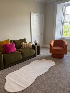 A living room with a green sofa, a white rug, a small table with a lamp, and a window with a view. - 2 bed homely central apartment (Edinburgh)