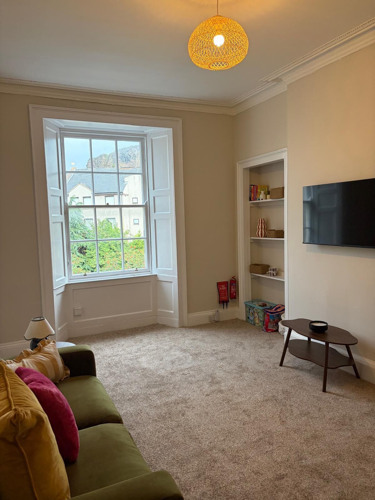 A room with a large window, a television mounted on the wall, and a small table.