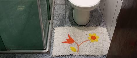 A bathroom with a toilet, a glass shower door, and a rug with a floral design.