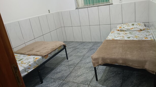 Um quarto pequeno, com azulejos, com duas camas, cada uma com colcha floral e manta marrom.