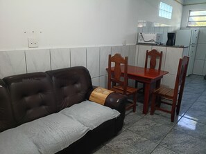 Un espacio de estar con un sofá marrón, una mesa de madera y dos sillas de madera.