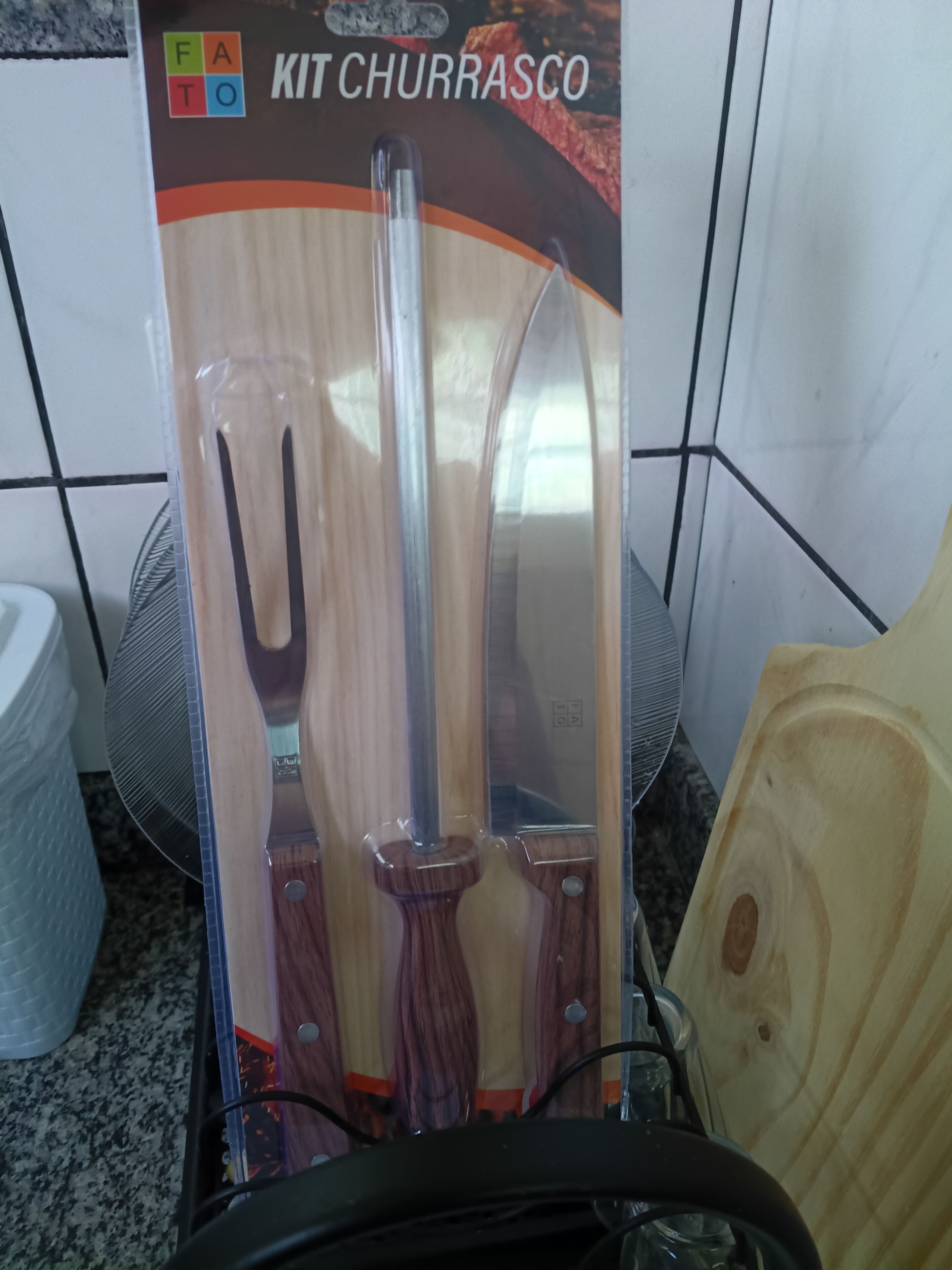 A kitchen with a box containing a churrasco kit, a knife, and a wooden cutting board.