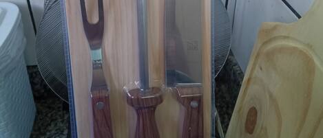 A kitchen with a box containing a churrasco kit, a knife, and a wooden cutting board.