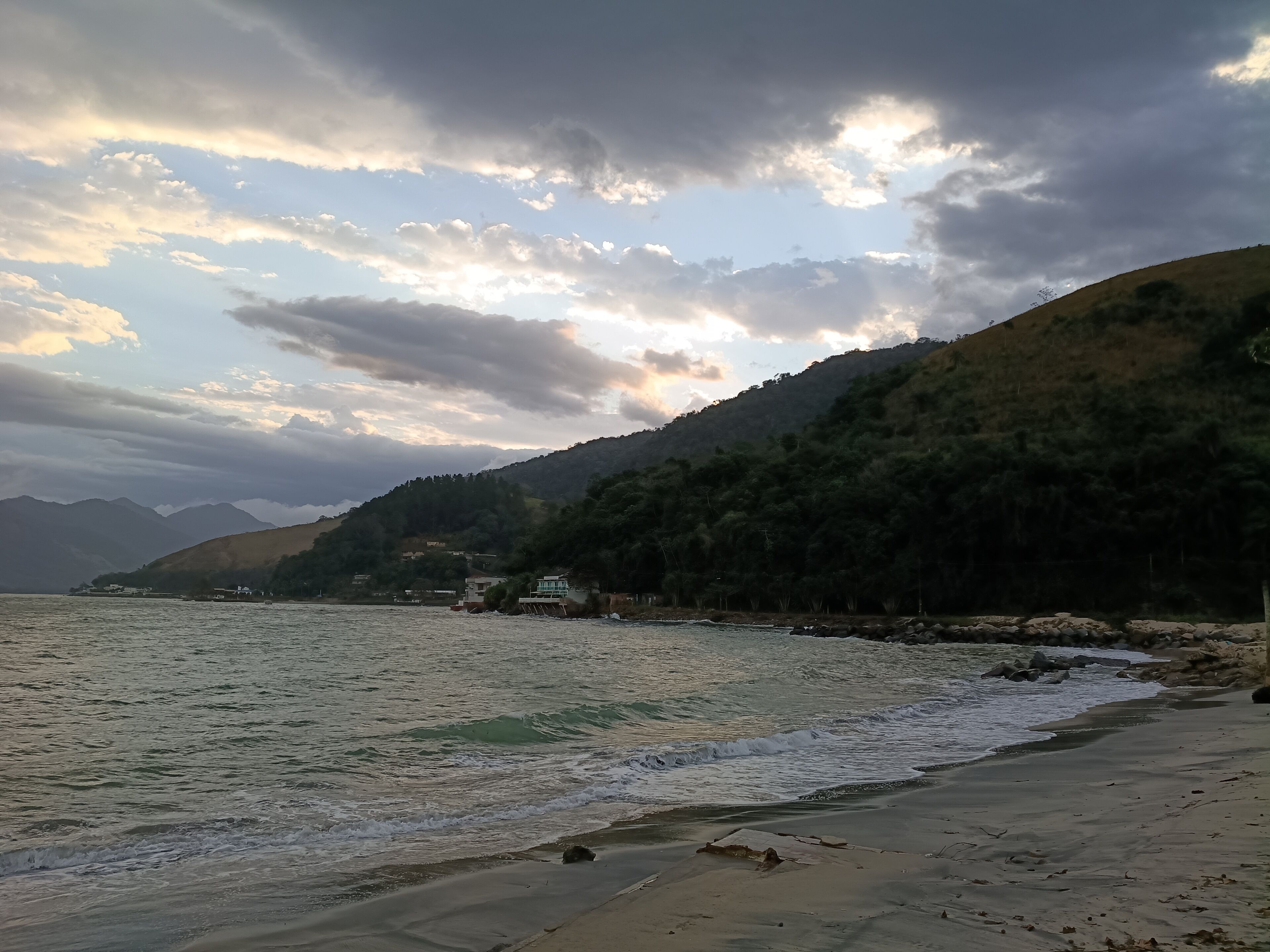 A coastal landscape with a beach, waves, and a mountain in the background.