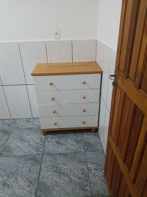 Ein weißer Kommode mit Holzköpfen und einer Holzplatte, vor einer gefliesten Wand mit einer Tür rechts.