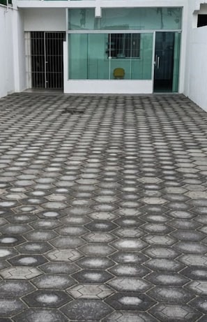 Ein sechseckig gemusterter Boden führt zu einem Gebäudeeingang mit einer Glastür und einem Metallgitter.