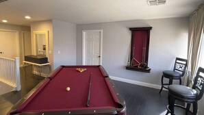 A pool table in a room with a door, a window with curtains, and a chair. - 5BR Pool House + Billiards · Up to 15 Guests (Las Vegas)