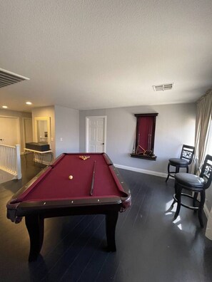 Une table de billard dans une pièce avec une porte, une fenêtre avec des rideaux et une chaise.