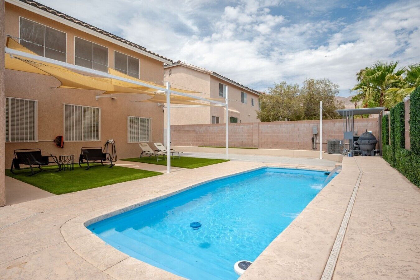 Uma piscina retangular com superfície de água azul translúcida, rodeada por um deck pavimentado.