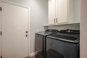 A laundry room with two front-loading washing machines and a white door. - 5BR Pool House + Billiards · Up to 15 Guests (Las Vegas)