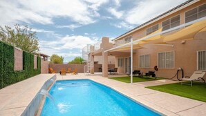 A swimming pool with a covered patio area, outdoor furniture, and a building with windows and a door. - 5BR Pool House + Billiards · Up to 15 Guests (Las Vegas)
