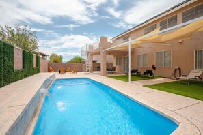 Une piscine avec un patio couvert, du mobilier d’extérieur et un bâtiment doté de fenêtres et d’une porte.