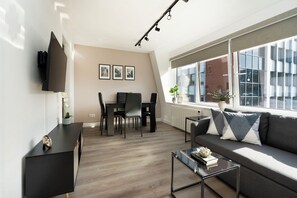 Un salon moderne comprenant un canapé, une table basse, un téléviseur, un coin repas et de grandes fenêtres.