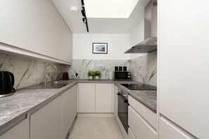 A modern kitchen with white cabinets, a microwave, a kettle, and a sink.
