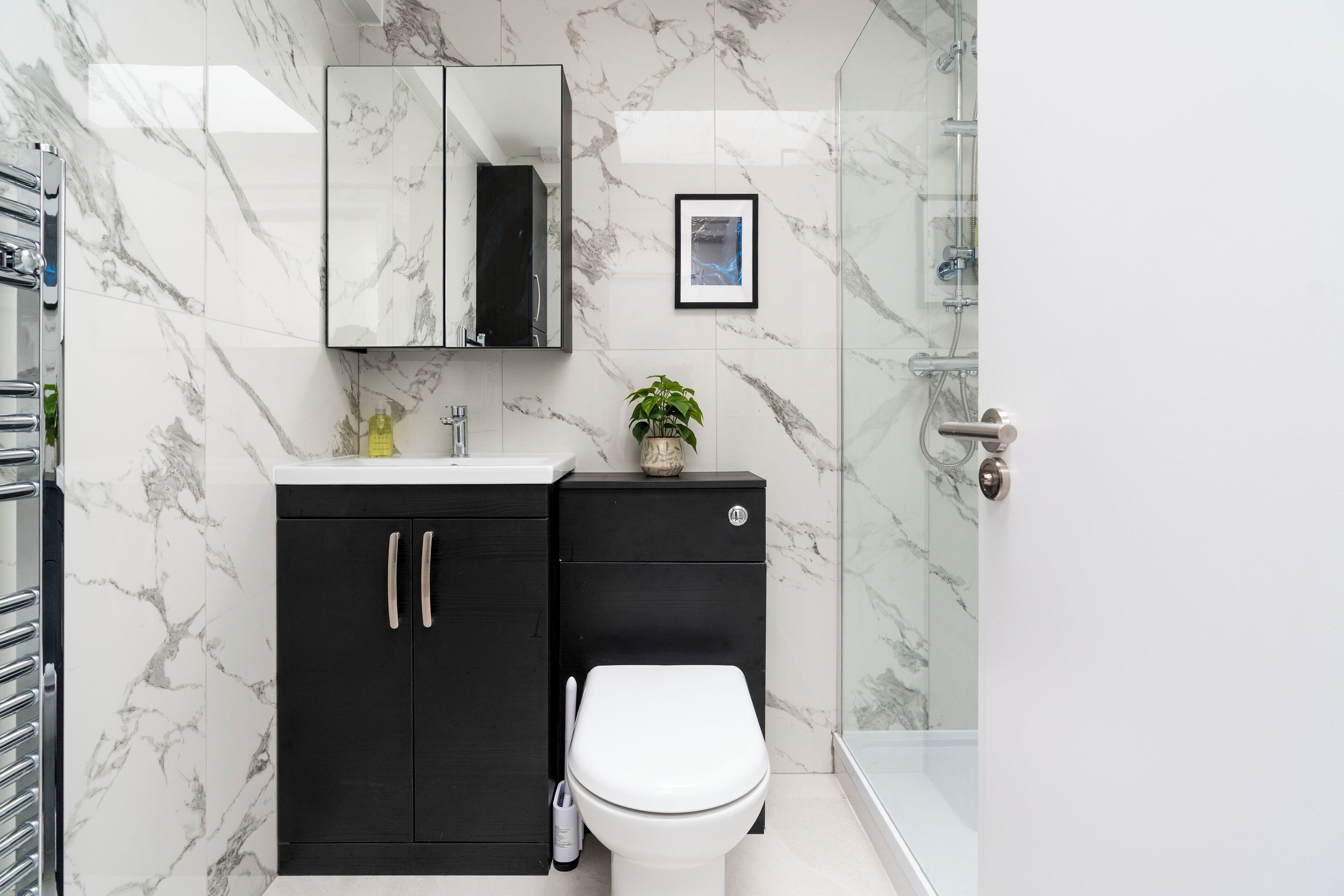 A bathroom with a marble wall, a black cabinet, a white toilet, a framed picture, and a shower area.