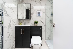 Une salle de bain avec un mur en marbre, un meuble noir, des toilettes blanches, un tableau encadré et un espace douche.
