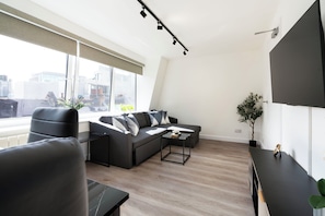 A modern living room with a sectional sofa, a black coffee table, a black armchair, and a large window with a view of buildings.