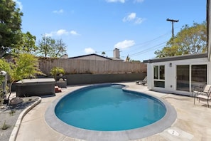A swimming pool with a curved edge, surrounded by a concrete deck. There are lounge chairs and a small table with a potted plant. - Beautiful Home in the Heart of San Diego! (San Diego)