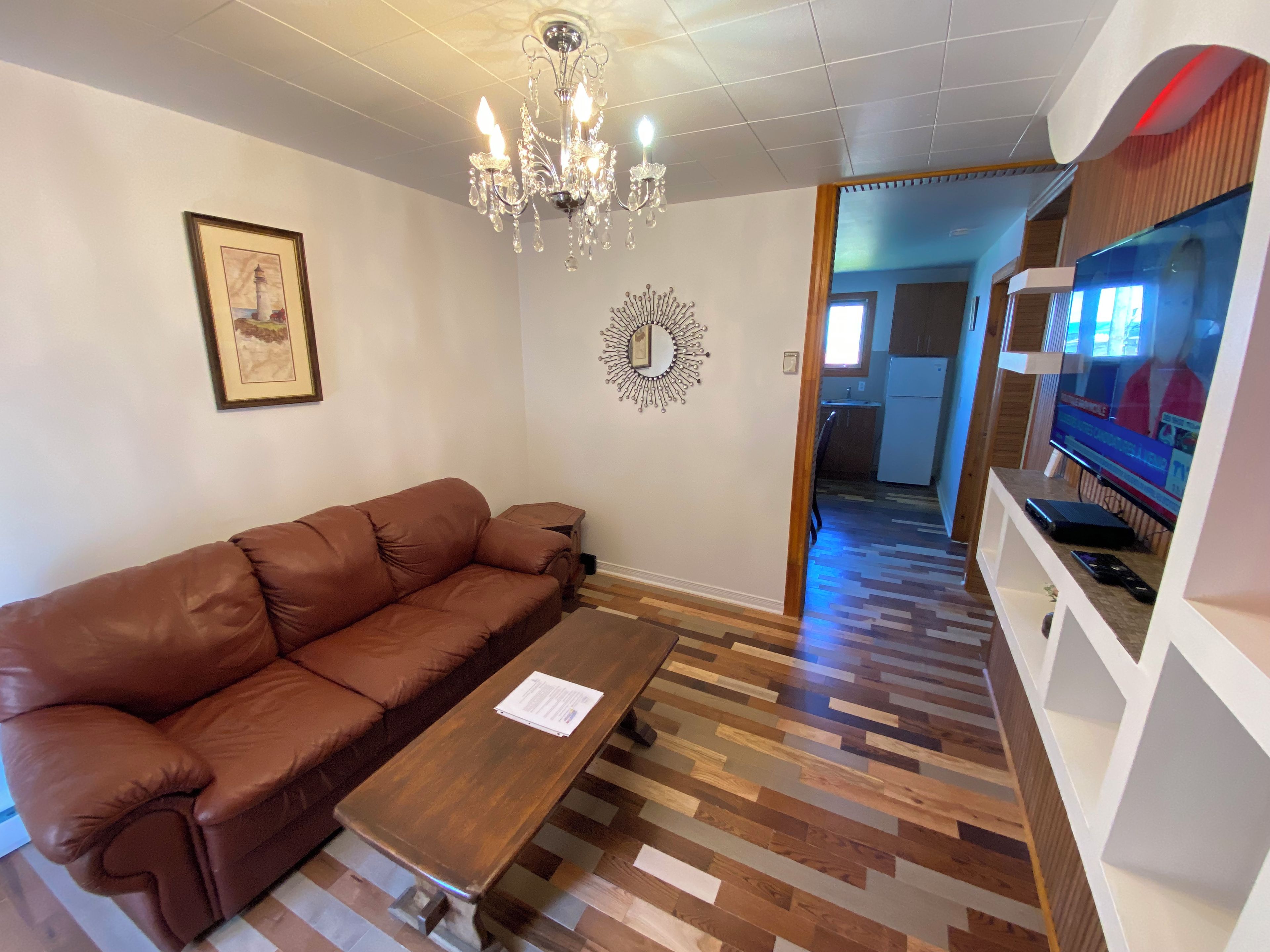 A living room with a brown leather sofa, a wooden coffee table, a chandelier, a framed picture, and a television.