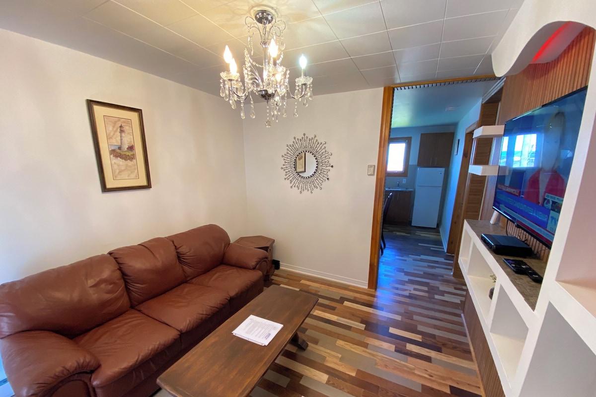 A living room with a brown leather sofa, a wooden coffee table, a chandelier, a framed picture, and a television.