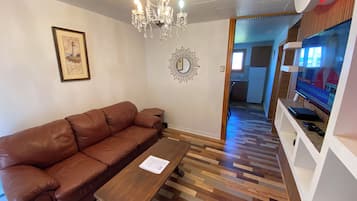 A living room with a brown leather sofa, a wooden coffee table, a chandelier, a framed picture, and a television.