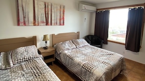 Une chambre d’hôtel avec deux lits, un ventilateur de plafond, un appareil de climatisation, une fenêtre avec des rideaux et une œuvre d’art accrochée au mur.
