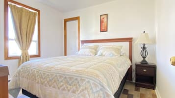 A bedroom with a bed, a nightstand, a lamp, a ceiling fan, and a window with curtains.