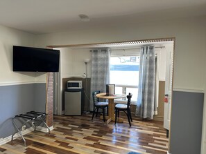 A room with a flat-screen TV, a microwave, a table with chairs, and a window with curtains.