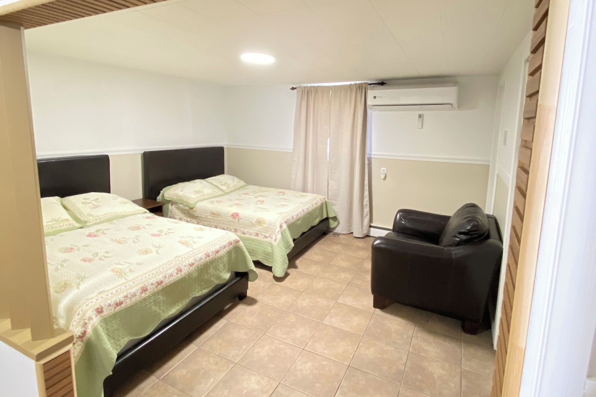 A bedroom with two beds, a sofa, an air conditioning unit, and a tiled floor.
