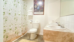 Une salle de bain équipée de toilettes, d’un lavabo, d’un rideau de douche et d’une œuvre d’art florale encadrée au mur.