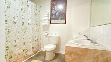 A bathroom with a toilet, sink, shower curtain, and a framed floral artwork on the wall.