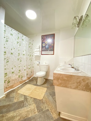 Un baño con inodoro, lavamanos, cortina de ducha y un cuadro floral enmarcado en la pared.