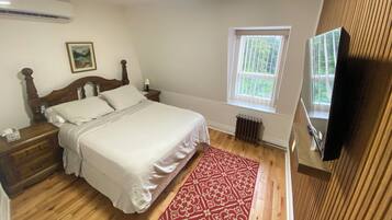 A bedroom with a bed, nightstands, a radiator, a window, and a television.