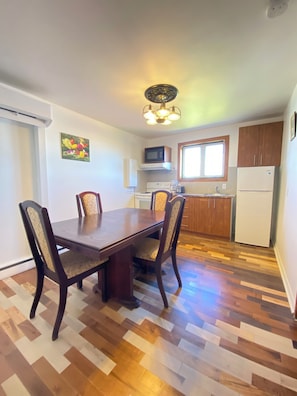 Un comedor con mesa y sillas de madera, una cocina con electrodomésticos y un ventanal.
