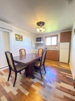 Un comedor con mesa y sillas de madera, una cocina con electrodomésticos y un ventanal.