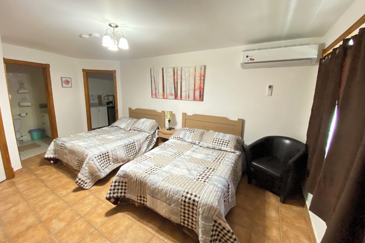 A hotel room with two beds, a bathroom, a ceiling fan, and an air conditioning unit.