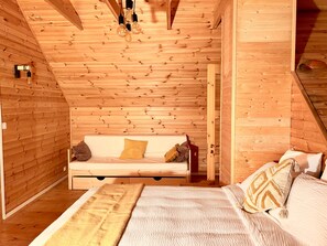 A cozy room with a wooden sloped ceiling, a bed with a white comforter, a wooden bench with cushions, and a small table with a lamp. - Chalet de la Garde - Alpe d'Huez Resort (La Garde)