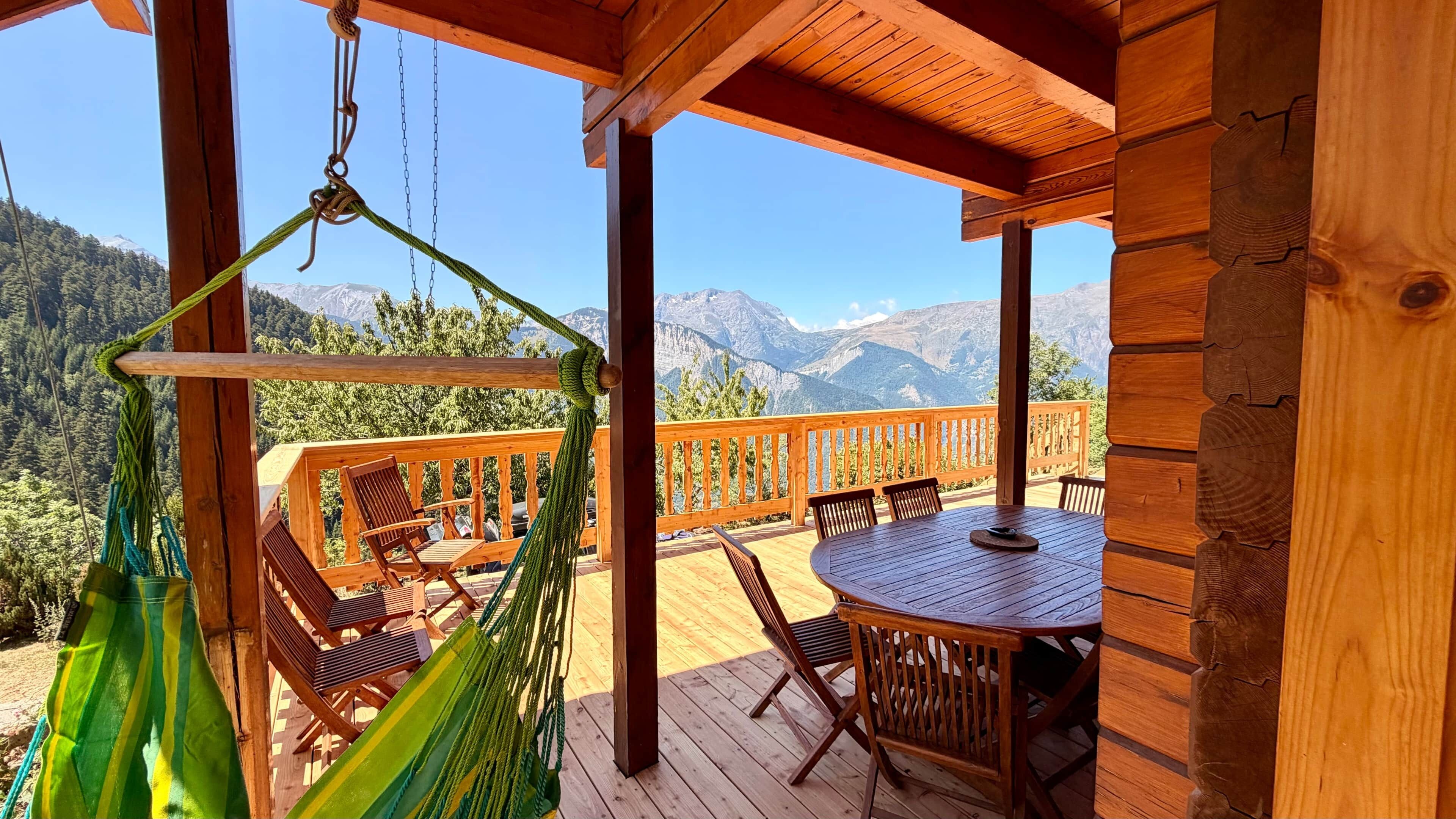 A wooden deck with a table and chairs, a hammock, and a view of mountains.