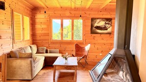A wooden cabin interior with a sofa, a table, a chair, and a fireplace. - Chalet de la Garde - Alpe d'Huez Resort (La Garde)