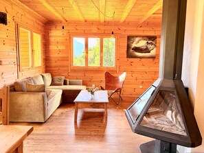 A wooden cabin interior with a sofa, a table, a chair, and a fireplace. - Chalet de la Garde - Alpe d'Huez Resort (La Garde)