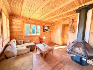 A wooden cabin interior with a sofa, a table, a fireplace, and a guitar. - Chalet de la Garde - Alpe d'Huez Resort (La Garde)