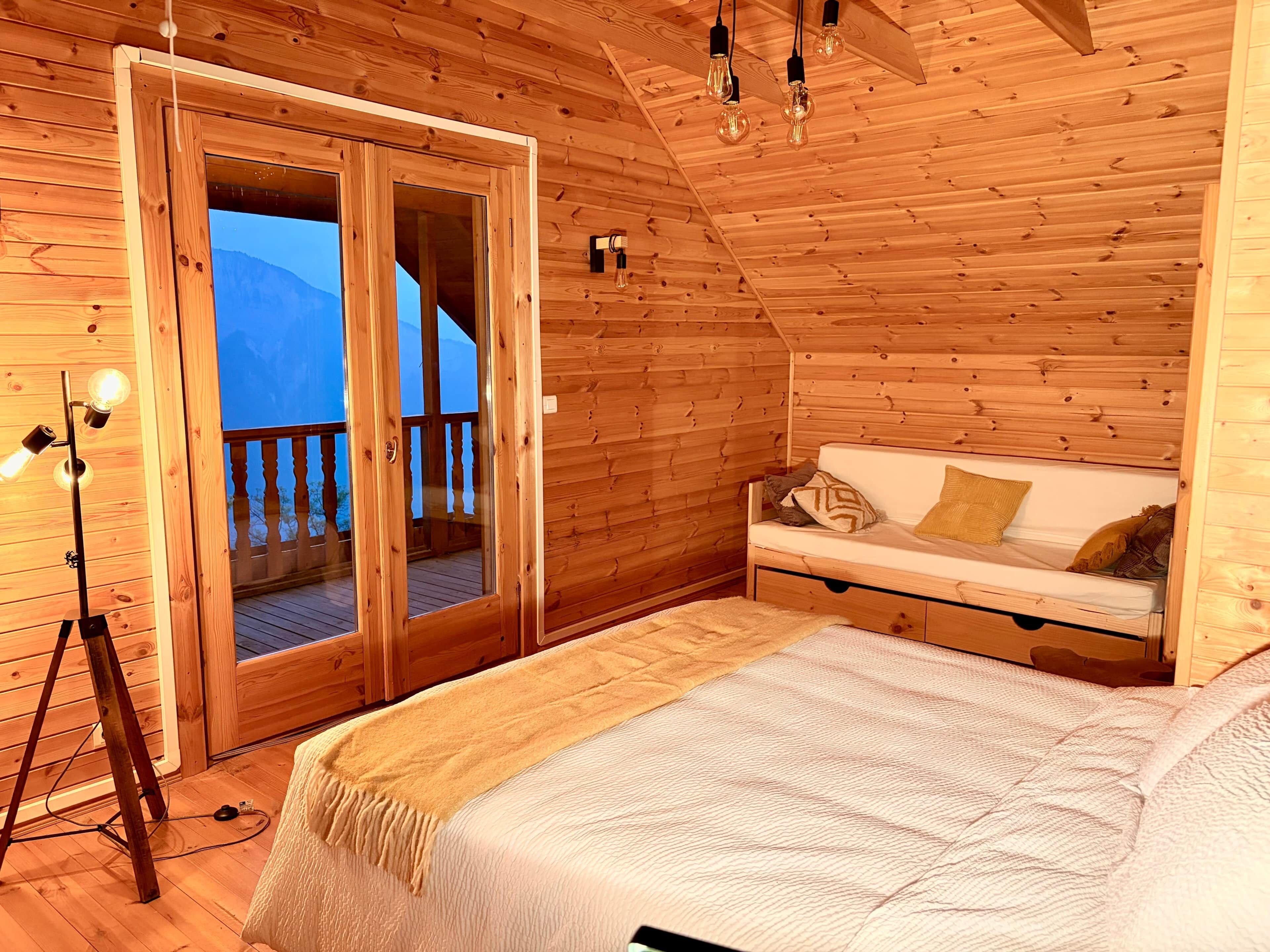 Een houten kamer met een bed, een bank en een schuifdeur naar een balkon.