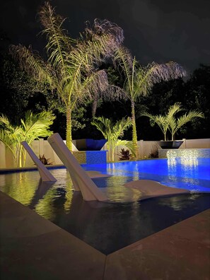 A swimming pool with a modern design, surrounded by palm trees and plants. - The Pearl Sunset Haven | Luxury Spa Retreat (Seminole)