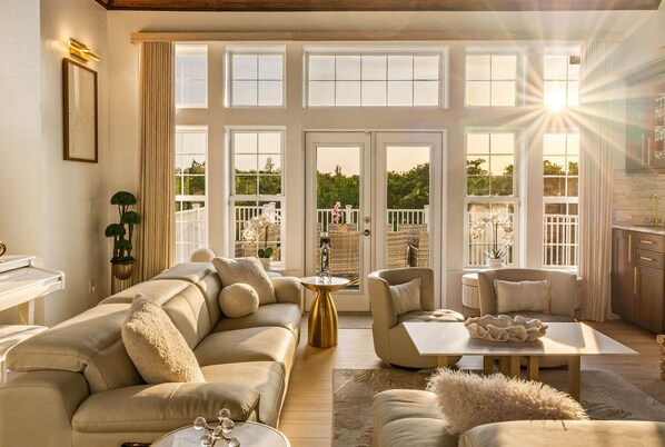 A spacious living room with a large sofa, a coffee table, and a view of the outdoors through large windows. - The Pearl Sunset Haven | Luxury Spa Retreat (Seminole)