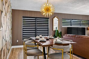 A dining area with a wooden table, four chairs, and a modern chandelier. - The '59 Flamingo | Pool, Hot Tub & Cold Plunge (Apollo Beach)