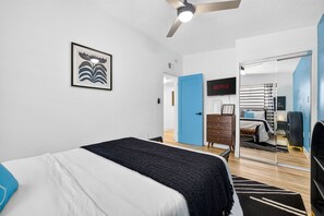 Ein modernes Schlafzimmer mit einem Bett, einer Kommode, einem Fernseher und einer Tür zu einem Badezimmer.