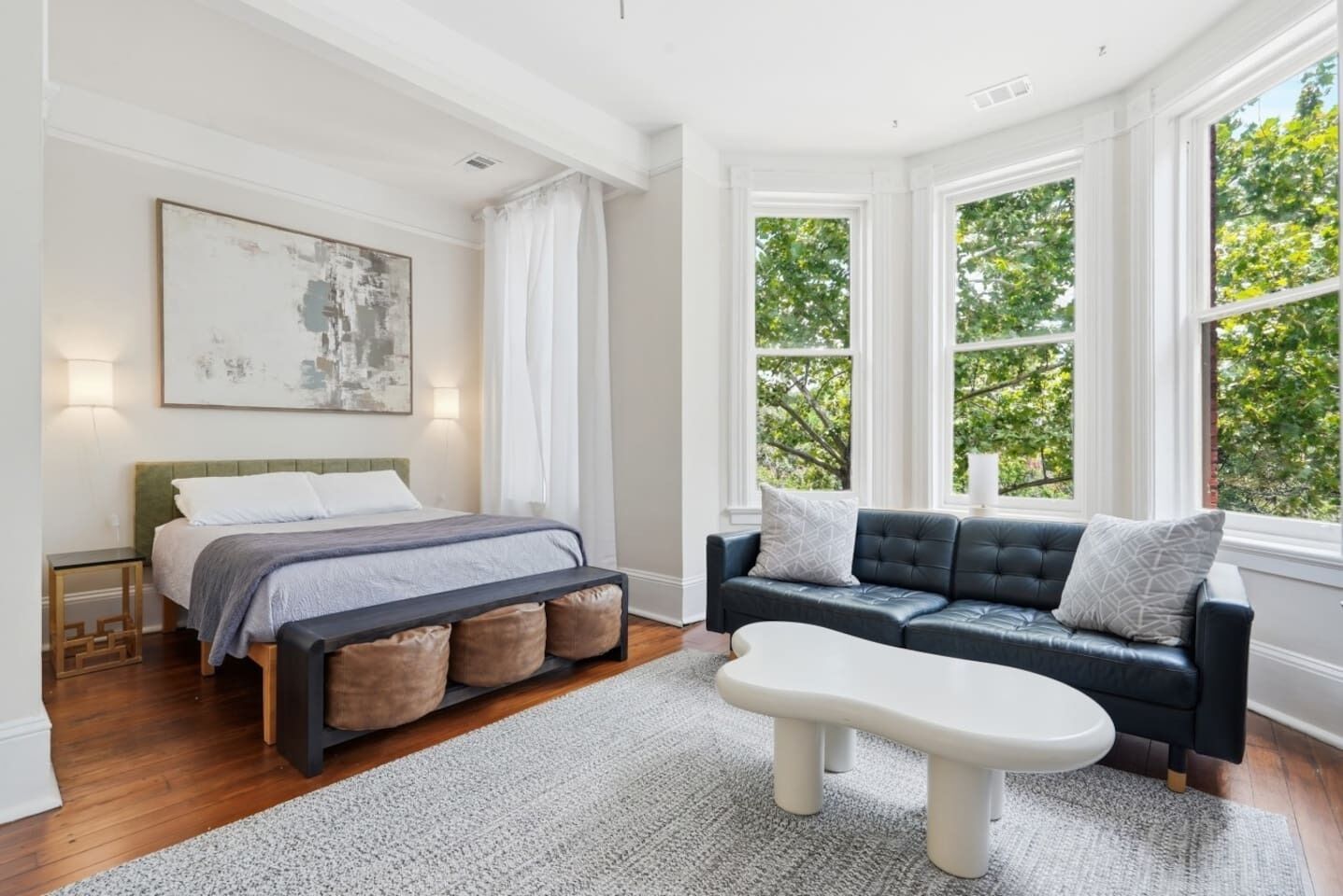 A bedroom with a bed, a sofa, a coffee table, and large windows with a view of trees.