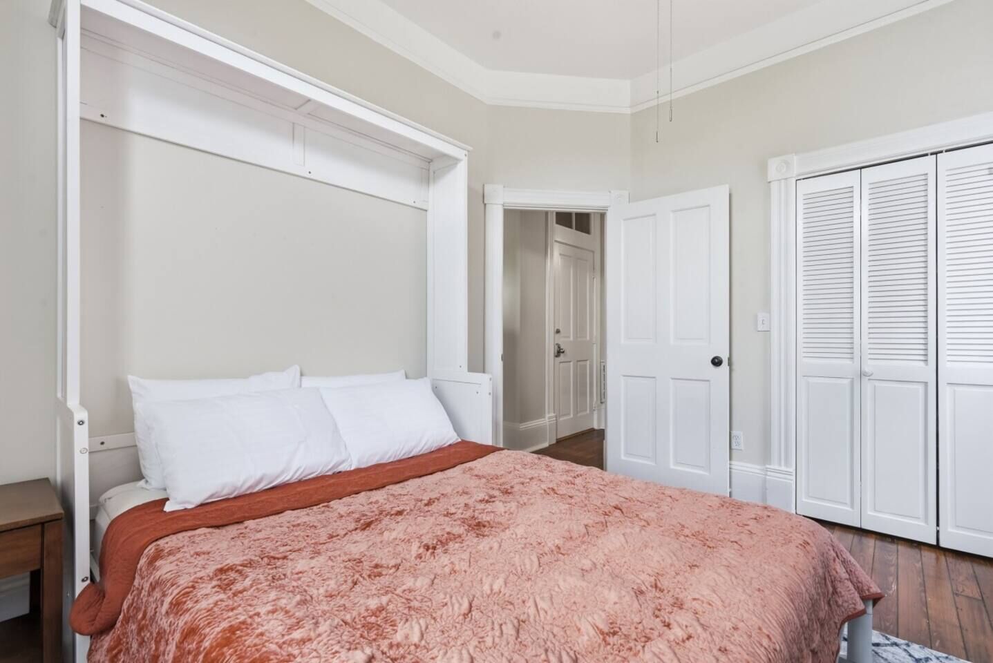 Une chambre à coucher avec un lit, une armoire blanche et une porte donnant sur une autre pièce.