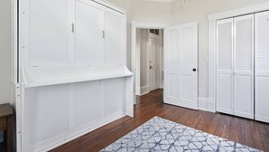 Un pasillo con armarios blancos, piso de madera y una alfombra estampada.